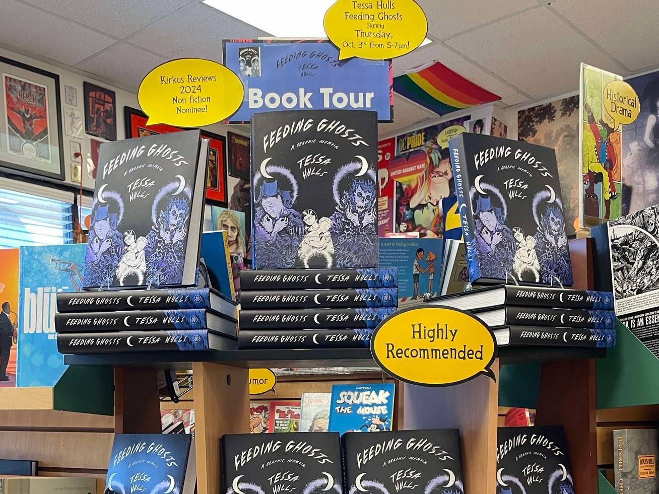 A bookstore display with stacks of a book titled "Feeding Ghosts" by Tessa Wolfe. The display includes promotional signs and balloons stating "Highly Recommended" and details about a book tour.