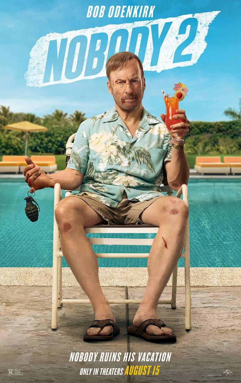 A man with a bruised face and bandaged knees sits on a poolside chair, holding a tropical drink; the poster promotes the film "Nobody 2," starring Bob Odenkirk.