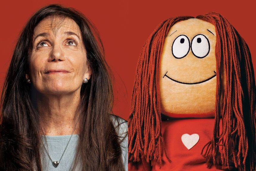 A woman with long brown hair looks up next to a smiling doll with long red yarn hair, both against a red background.